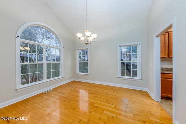 unfurnished dining area featuring light hardwood / wood-style flooring, high vaulted ceiling, and an inviting chandelier