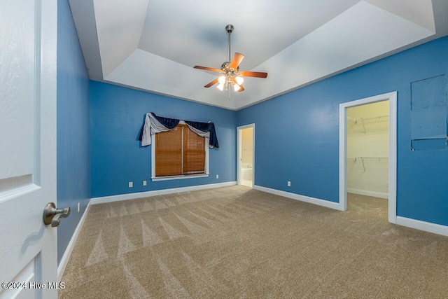 unfurnished bedroom with a raised ceiling, a walk in closet, carpet flooring, ceiling fan, and a closet