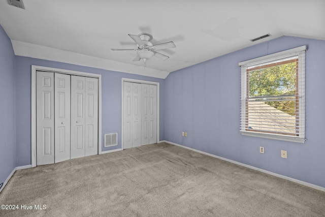 unfurnished bedroom featuring lofted ceiling, ceiling fan, light carpet, and two closets