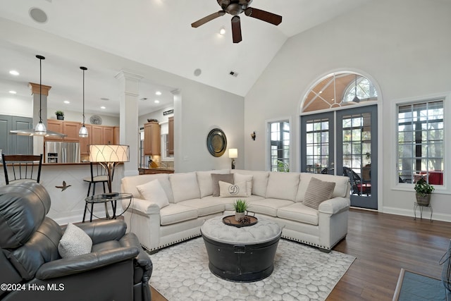 living room with decorative columns, ceiling fan, high vaulted ceiling, and dark wood-type flooring