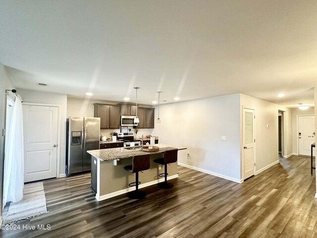 kitchen with hanging light fixtures, appliances with stainless steel finishes, a kitchen island with sink, and dark wood-type flooring