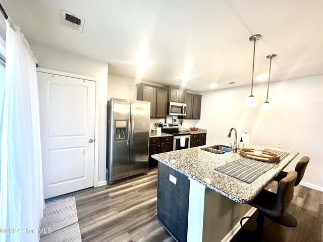 kitchen with light stone countertops, appliances with stainless steel finishes, a kitchen breakfast bar, dark wood-type flooring, and hanging light fixtures