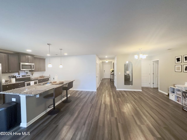 kitchen featuring a kitchen breakfast bar, an island with sink, appliances with stainless steel finishes, decorative light fixtures, and dark hardwood / wood-style flooring