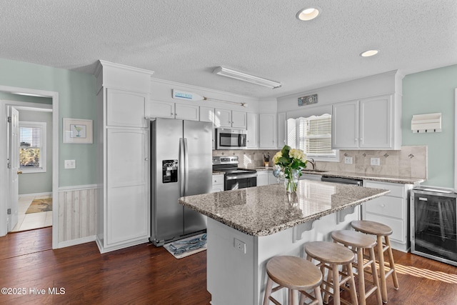 kitchen featuring stainless steel appliances, white cabinets, a textured ceiling, a center island, and beverage cooler