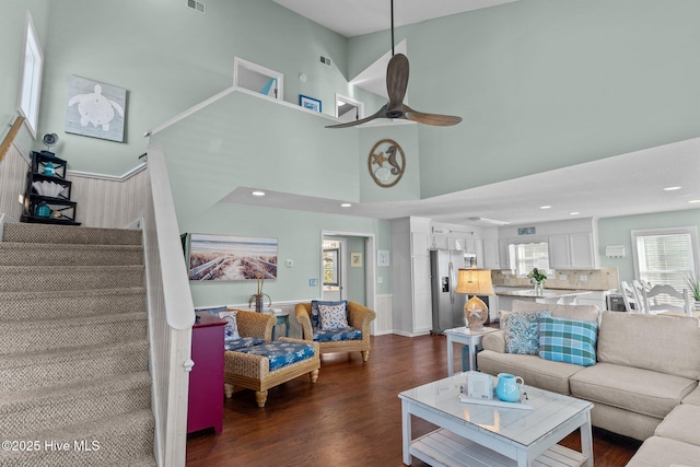 living room with a towering ceiling, ceiling fan, and dark hardwood / wood-style flooring