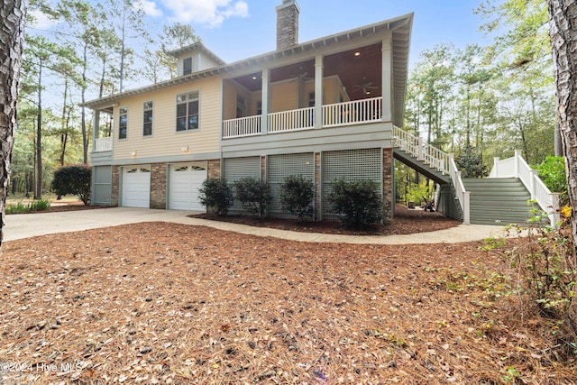 exterior space with a chimney, concrete driveway, an attached garage, ceiling fan, and stairs