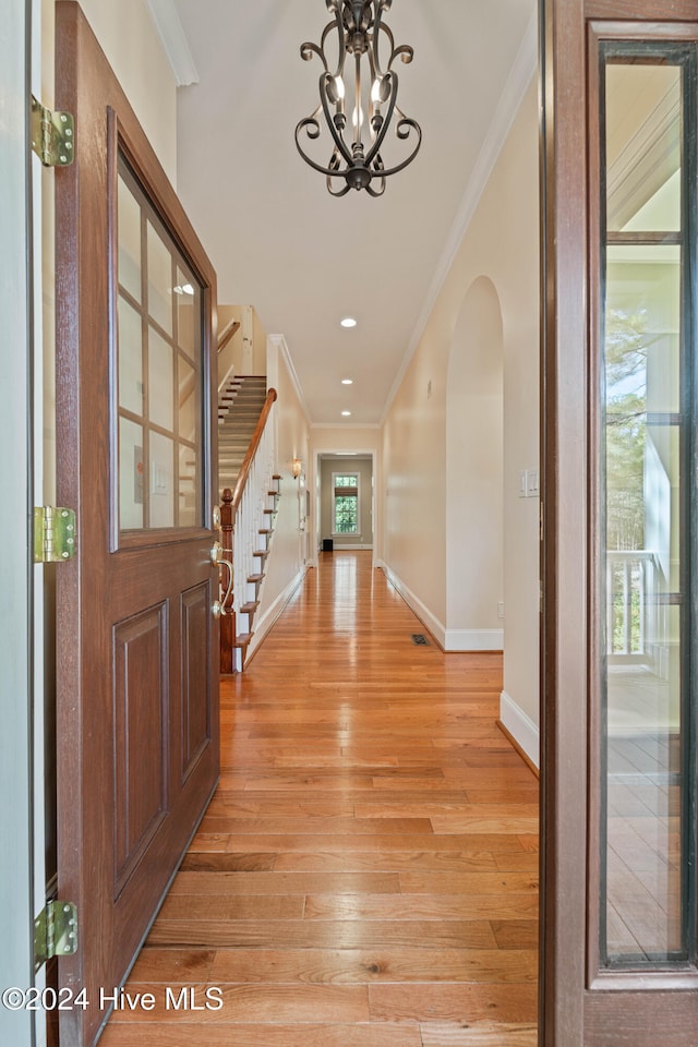 foyer entrance featuring a notable chandelier, crown molding, light wood-style floors, baseboards, and stairs