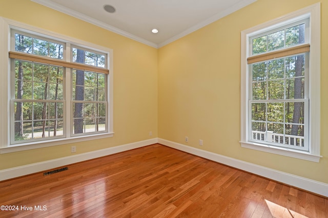 empty room with ornamental molding, visible vents, baseboards, and hardwood / wood-style flooring