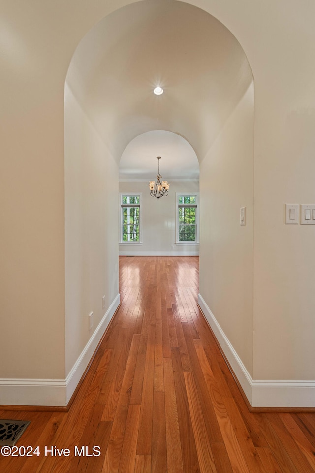 corridor featuring a chandelier, arched walkways, light wood-style flooring, and baseboards