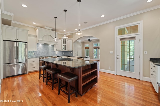 kitchen featuring arched walkways, tasteful backsplash, ornamental molding, high quality fridge, and a kitchen bar