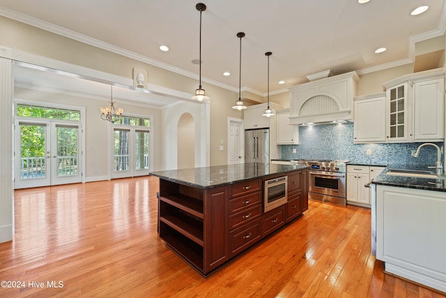 kitchen with a sink, high quality appliances, white cabinets, light wood-type flooring, and backsplash