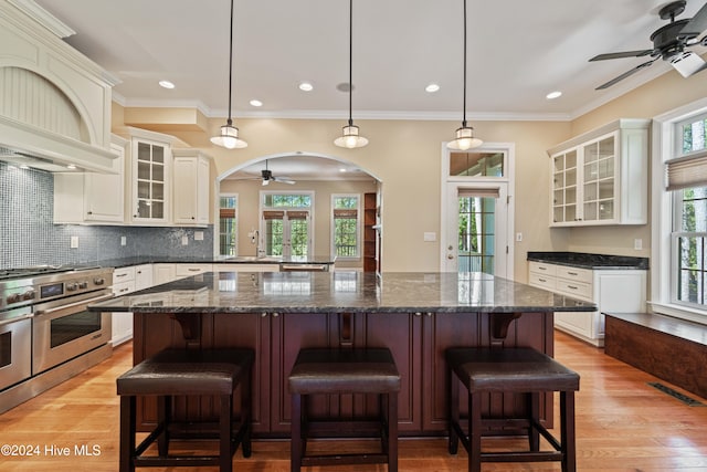 kitchen featuring light wood-type flooring, arched walkways, stainless steel range, and decorative backsplash