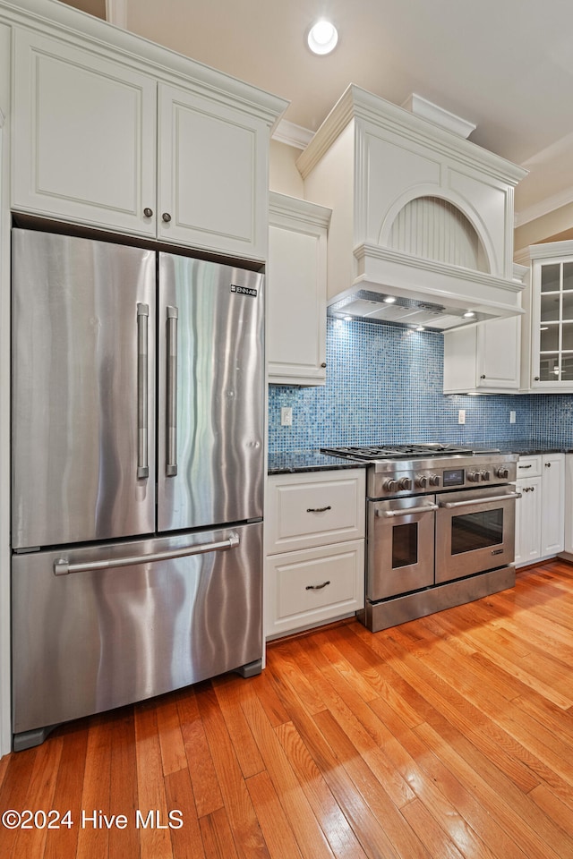 kitchen with white cabinets, premium appliances, ornamental molding, light wood-type flooring, and backsplash