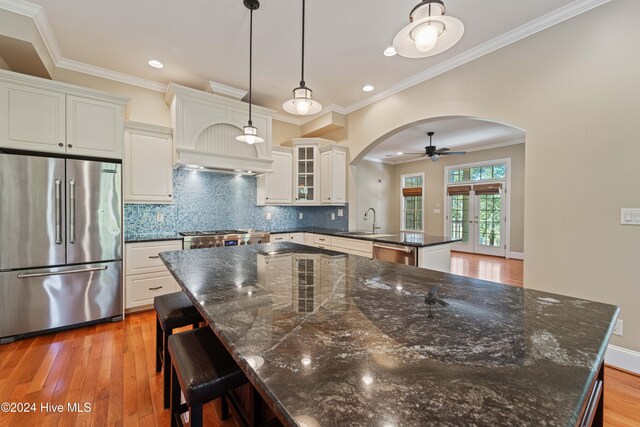 kitchen with arched walkways, appliances with stainless steel finishes, a peninsula, light wood-type flooring, and a sink