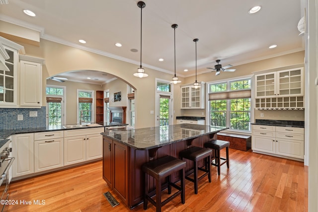 kitchen with a center island, visible vents, decorative backsplash, light wood-style floors, and glass insert cabinets