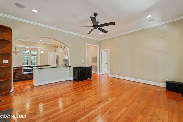 unfurnished living room with light wood-style floors, baseboards, arched walkways, and crown molding