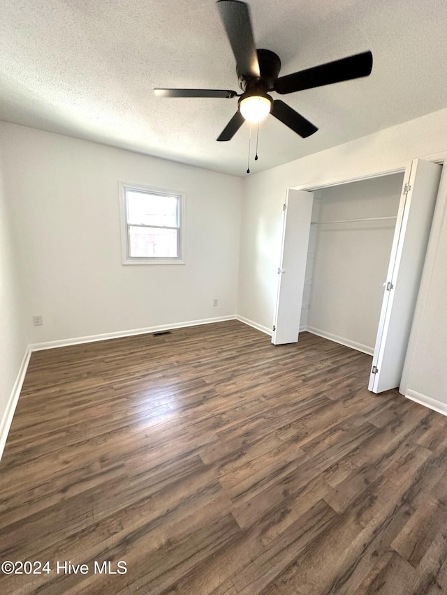 unfurnished bedroom featuring a textured ceiling, ceiling fan, dark wood-type flooring, and a closet