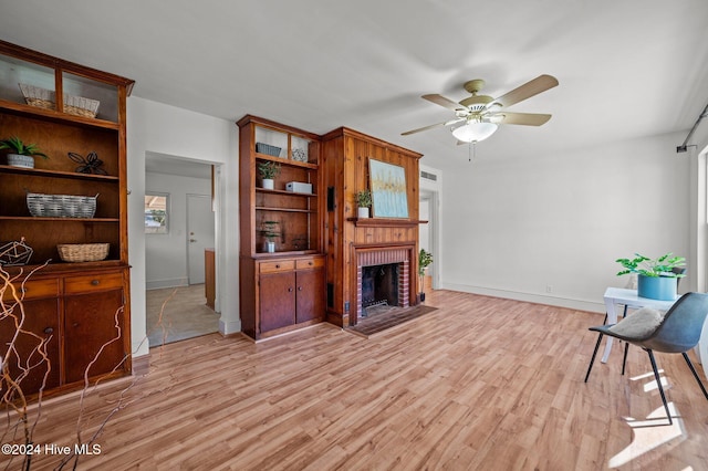 living room featuring ceiling fan, light hardwood / wood-style floors, and a brick fireplace