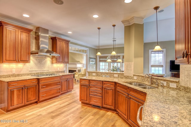 kitchen with decorative light fixtures, wall chimney range hood, sink, and light hardwood / wood-style flooring