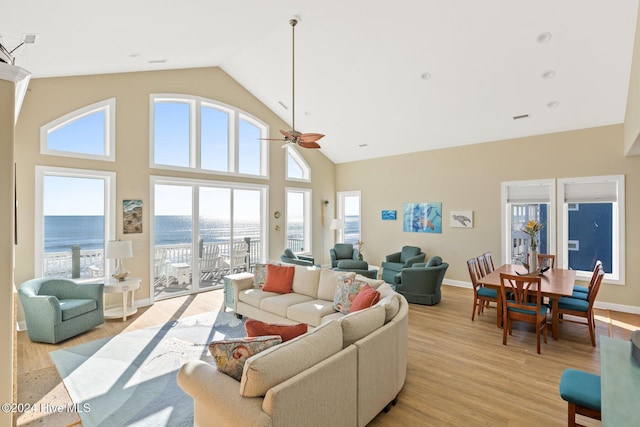 living room with ceiling fan, a water view, high vaulted ceiling, and light hardwood / wood-style floors