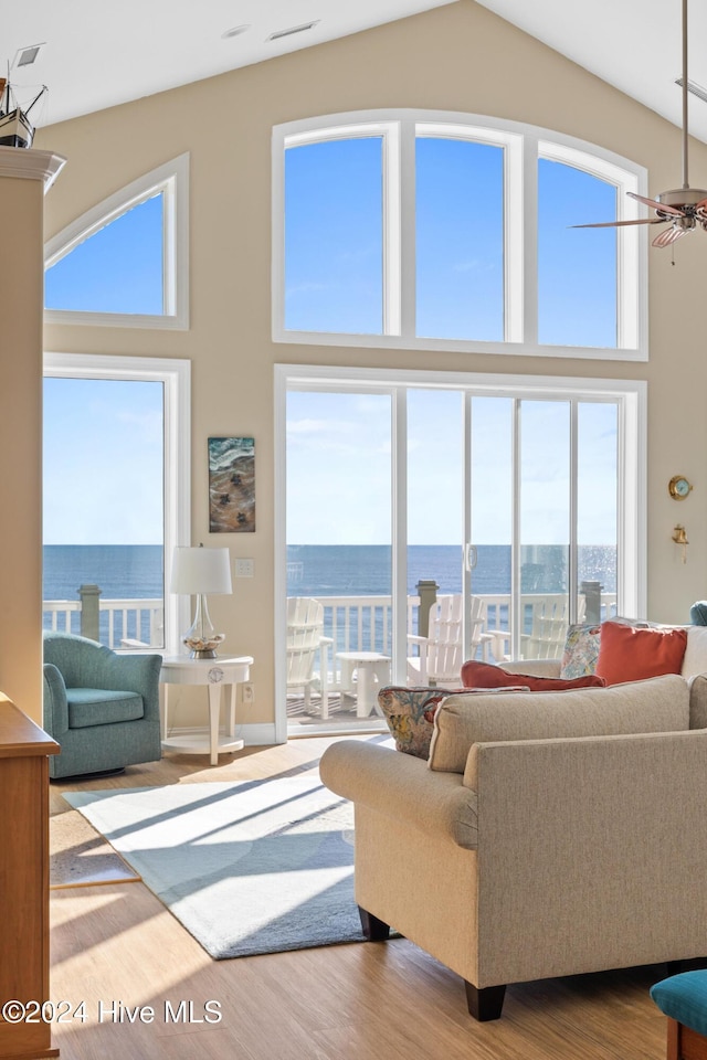 living room featuring a high ceiling, light hardwood / wood-style flooring, ceiling fan, and a water view