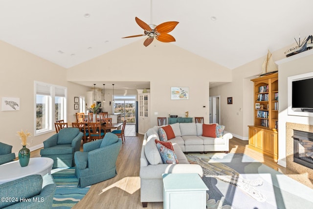 living room featuring ceiling fan, high vaulted ceiling, a premium fireplace, and light hardwood / wood-style floors