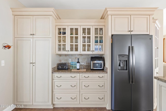 kitchen featuring cream cabinetry, decorative backsplash, dark stone counters, and stainless steel fridge with ice dispenser