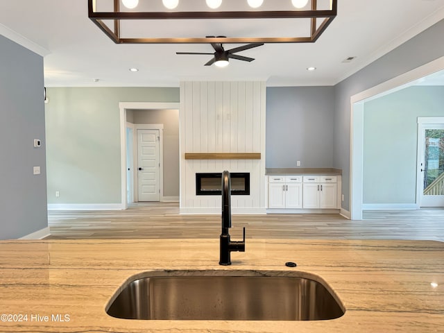 kitchen featuring white cabinets, light wood-type flooring, a large fireplace, and sink