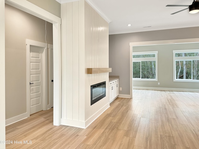 unfurnished living room with light wood-type flooring, a large fireplace, ceiling fan, and crown molding