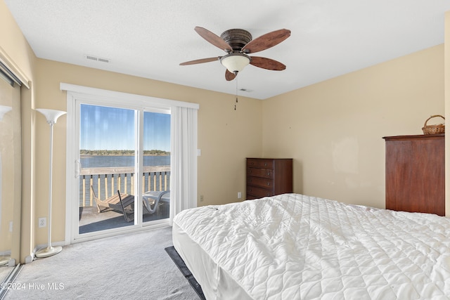 bedroom featuring access to outside, a water view, ceiling fan, a textured ceiling, and light colored carpet