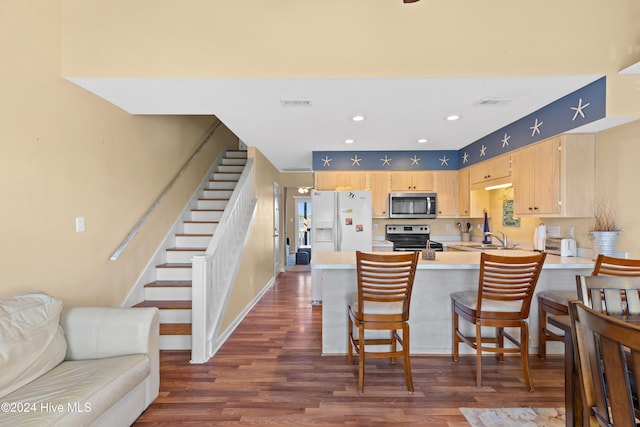 kitchen with stainless steel appliances, a kitchen breakfast bar, dark hardwood / wood-style flooring, kitchen peninsula, and light brown cabinetry