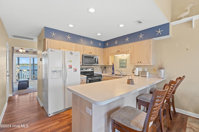 kitchen with wood-type flooring, kitchen peninsula, light brown cabinetry, and appliances with stainless steel finishes