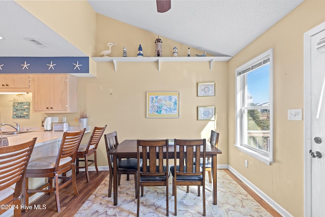 dining room featuring a textured ceiling, light hardwood / wood-style flooring, lofted ceiling, and sink