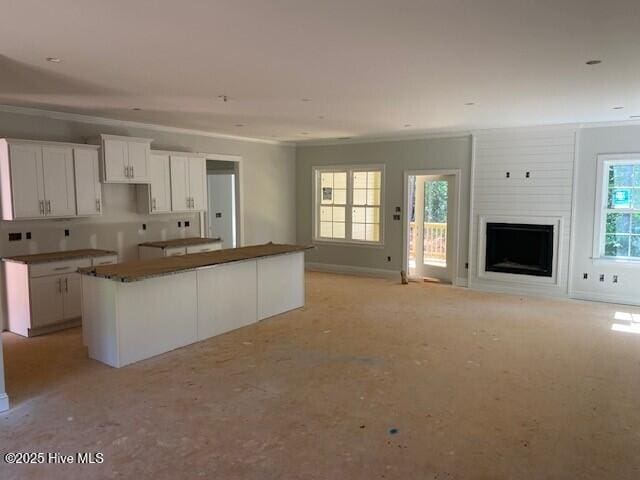 kitchen with white cabinets, open floor plan, a kitchen island, a fireplace, and ornamental molding