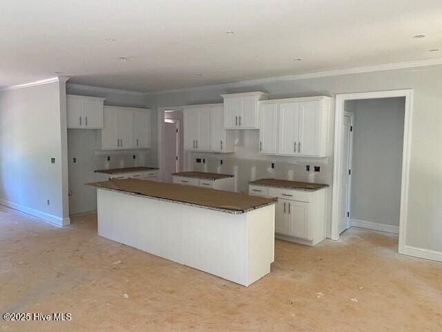 kitchen with a kitchen island, crown molding, baseboards, and white cabinets