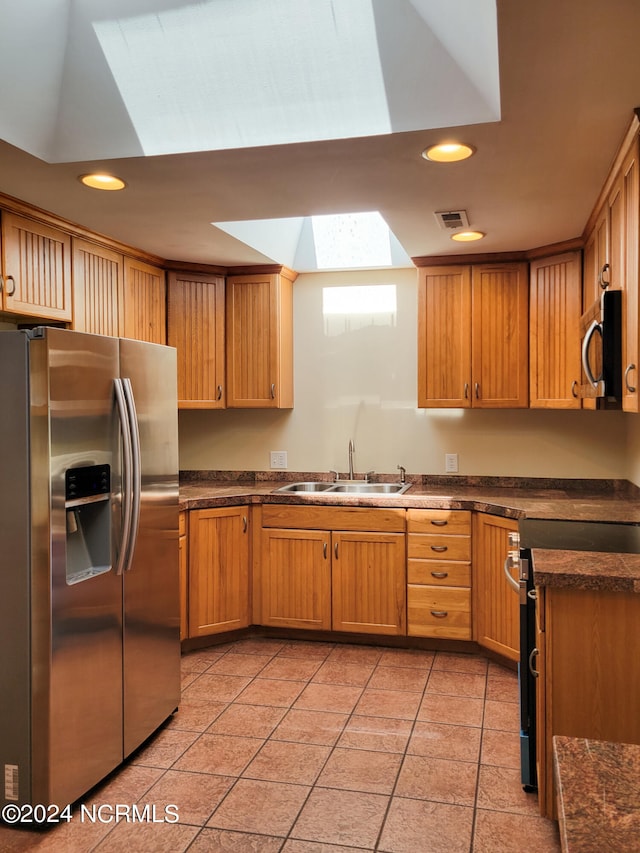 kitchen featuring a skylight, sink, light tile patterned flooring, and stainless steel appliances