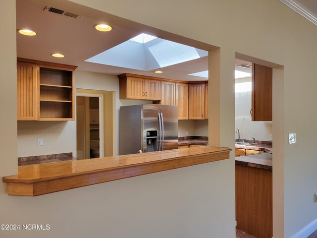 kitchen featuring a skylight, stainless steel fridge with ice dispenser, kitchen peninsula, and sink