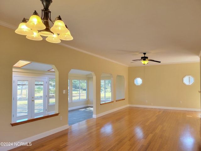 spare room featuring ceiling fan with notable chandelier, wood-type flooring, crown molding, and french doors