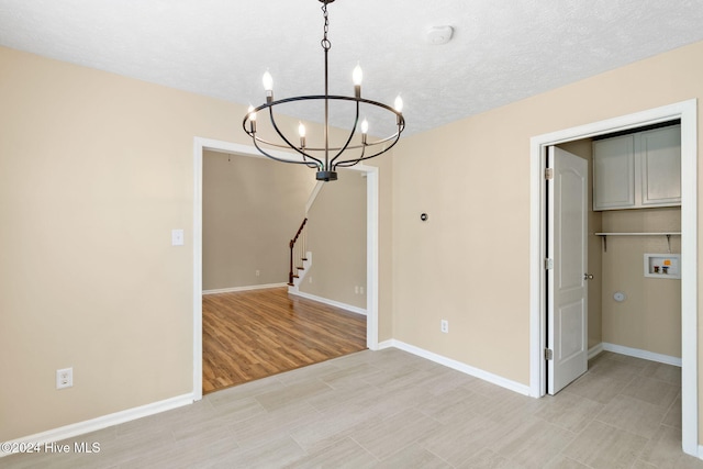 unfurnished dining area with a textured ceiling, a notable chandelier, and light wood-type flooring