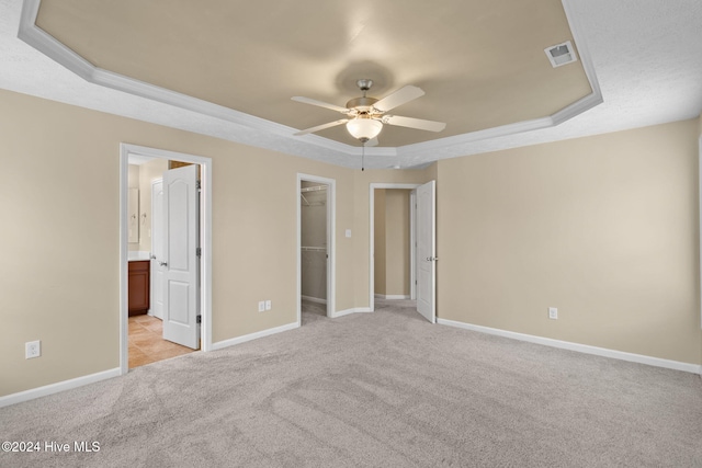 unfurnished bedroom featuring a spacious closet, ceiling fan, a tray ceiling, light carpet, and a closet