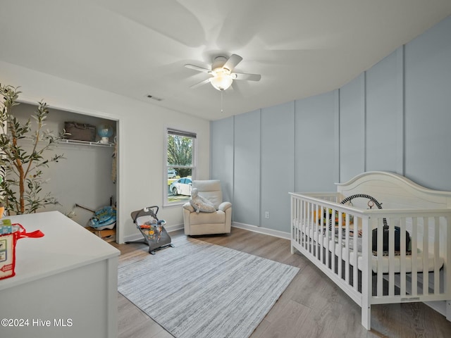 bedroom featuring light wood-type flooring, a nursery area, and ceiling fan