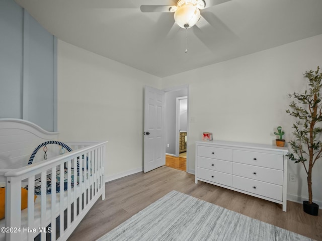 bedroom with ceiling fan, a nursery area, and light hardwood / wood-style flooring