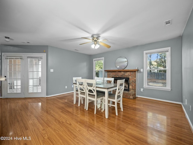 dining room featuring light wood-type flooring, a brick fireplace, a wealth of natural light, and ceiling fan