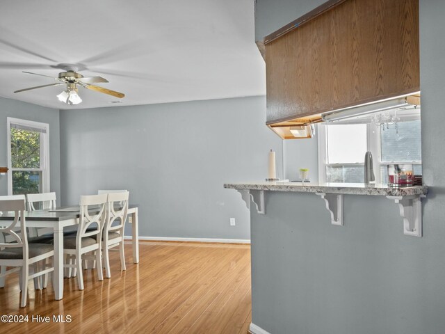 kitchen with a kitchen breakfast bar, light hardwood / wood-style floors, kitchen peninsula, and ceiling fan