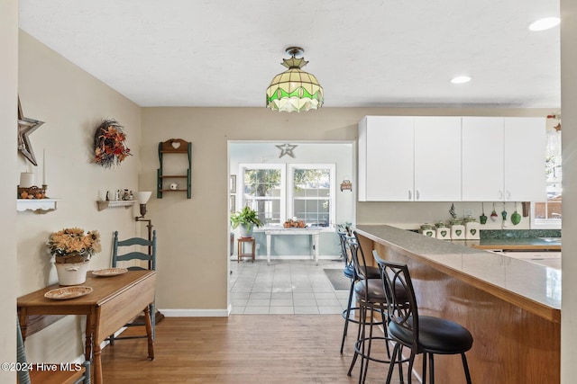 kitchen featuring kitchen peninsula, light hardwood / wood-style floors, white cabinetry, and hanging light fixtures