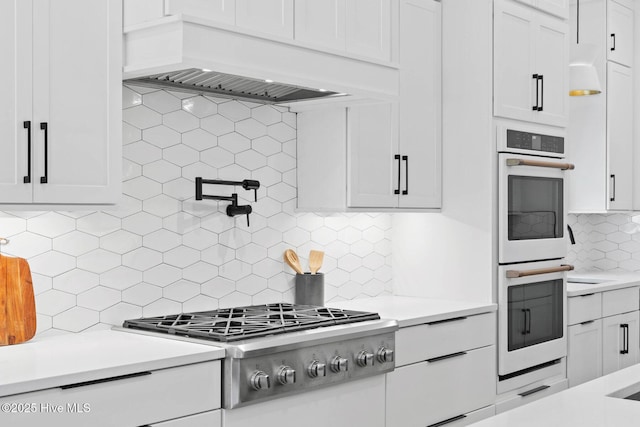 kitchen with stainless steel gas stovetop, tasteful backsplash, light countertops, and double oven