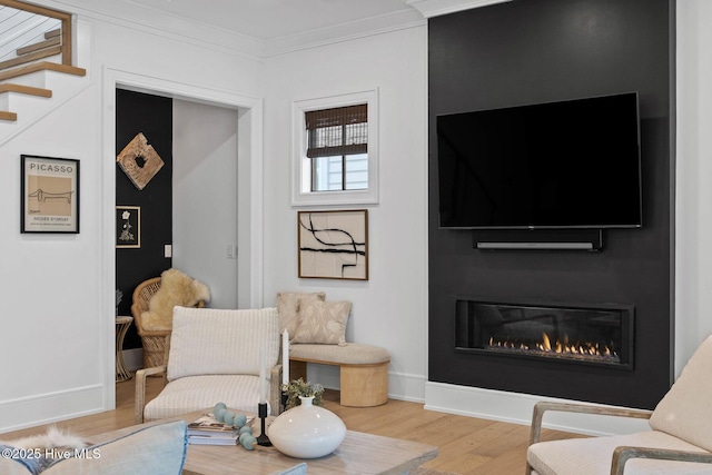 living area with crown molding, wood finished floors, baseboards, and a glass covered fireplace