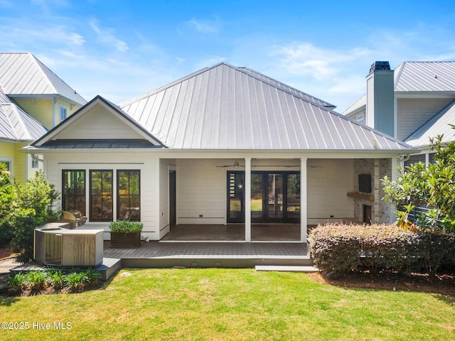 back of house with a chimney, metal roof, a deck, a lawn, and a standing seam roof