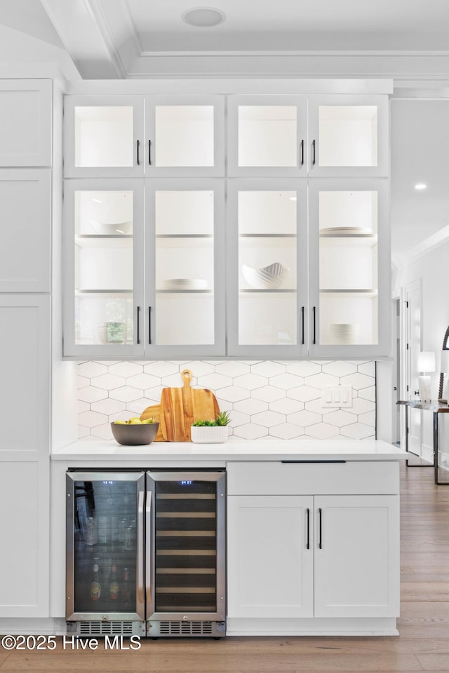 bar featuring light wood-style floors, crown molding, backsplash, and beverage cooler