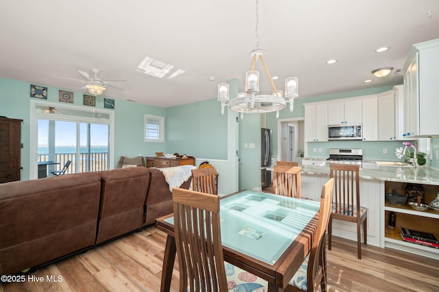 dining area with ceiling fan with notable chandelier, light wood-type flooring, a water view, and recessed lighting